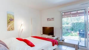 Une chambre à coucher comprenant un lit, un téléviseur et une porte-fenêtre coulissante donnant sur un espace extérieur.