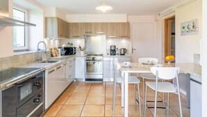 Une cuisine moderne dotée d’un îlot central, d’appareils électroménagers en acier inoxydable et d’un coin repas avec des chaises blanches.