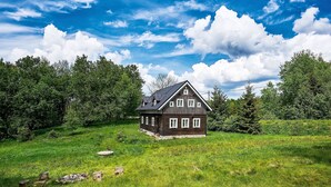 A wooden house with a sloped roof, surrounded by lush green grass and trees. - Sluneční vršek by Interhome (Kořenov)