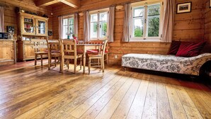 A wooden cabin interior with a dining table, chairs, a sofa, and a kitchen area. - Sluneční vršek by Interhome (Kořenov)