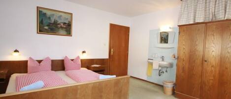 Un dormitorio con cama de madera, un cuadro en la pared, un armario de madera y un baño con lavabo y espejo.