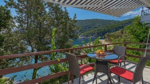 A balcony with wicker chairs and a table, overlooking a scenic coastal view with trees and hills. - Martina by Interhome (Hvar/Pokrivenik)