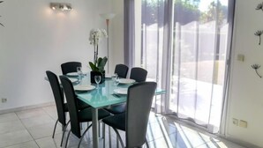 Un espace de salle à manger moderne avec une table en verre, des chaises noires et une vue sur l’extérieur grâce à de grandes fenêtres.