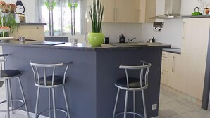 Une cuisine moderne dotée d’un îlot central, de tabourets de bar et de meubles de couleur claire.