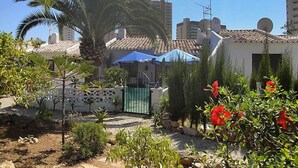 Un quartier résidentiel avec un palmier, un parasol bleu et un bâtiment blanc doté d’un toit en tuiles.