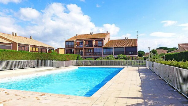 Una piscina con bordo piastrellato, circondata da una recinzione bianca e vegetazione.