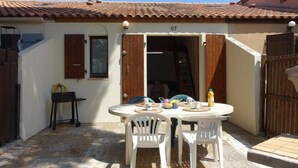 Un patio con un tavolo rotondo e sedie, una recinzione in legno e un edificio con tetto in tegole e numero 67.