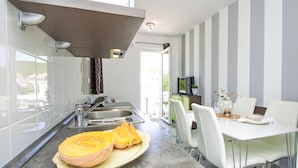 Una cocina moderna con una isla grande, electrodomésticos de acero inoxidable y un comedor con sillas blancas y una mesa de vidrio.