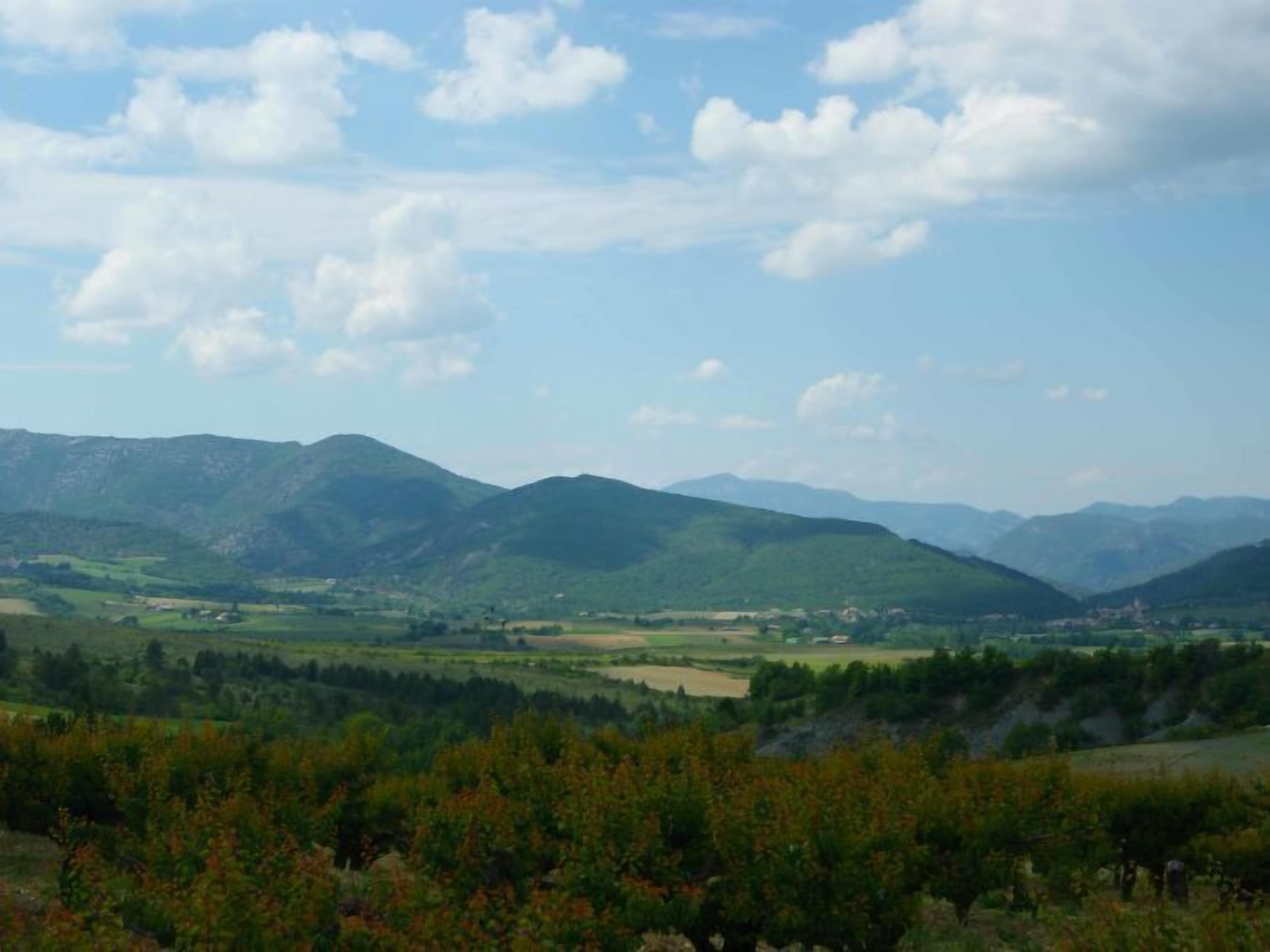 Un paysage montagneux avec une vallée et quelques bâtiments dispersés.