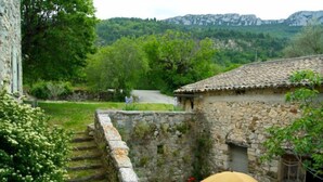 Un bâtiment en pierre avec un toit en tuiles, un mur en pierre et un jardin agrémenté de fleurs et d’un banc.