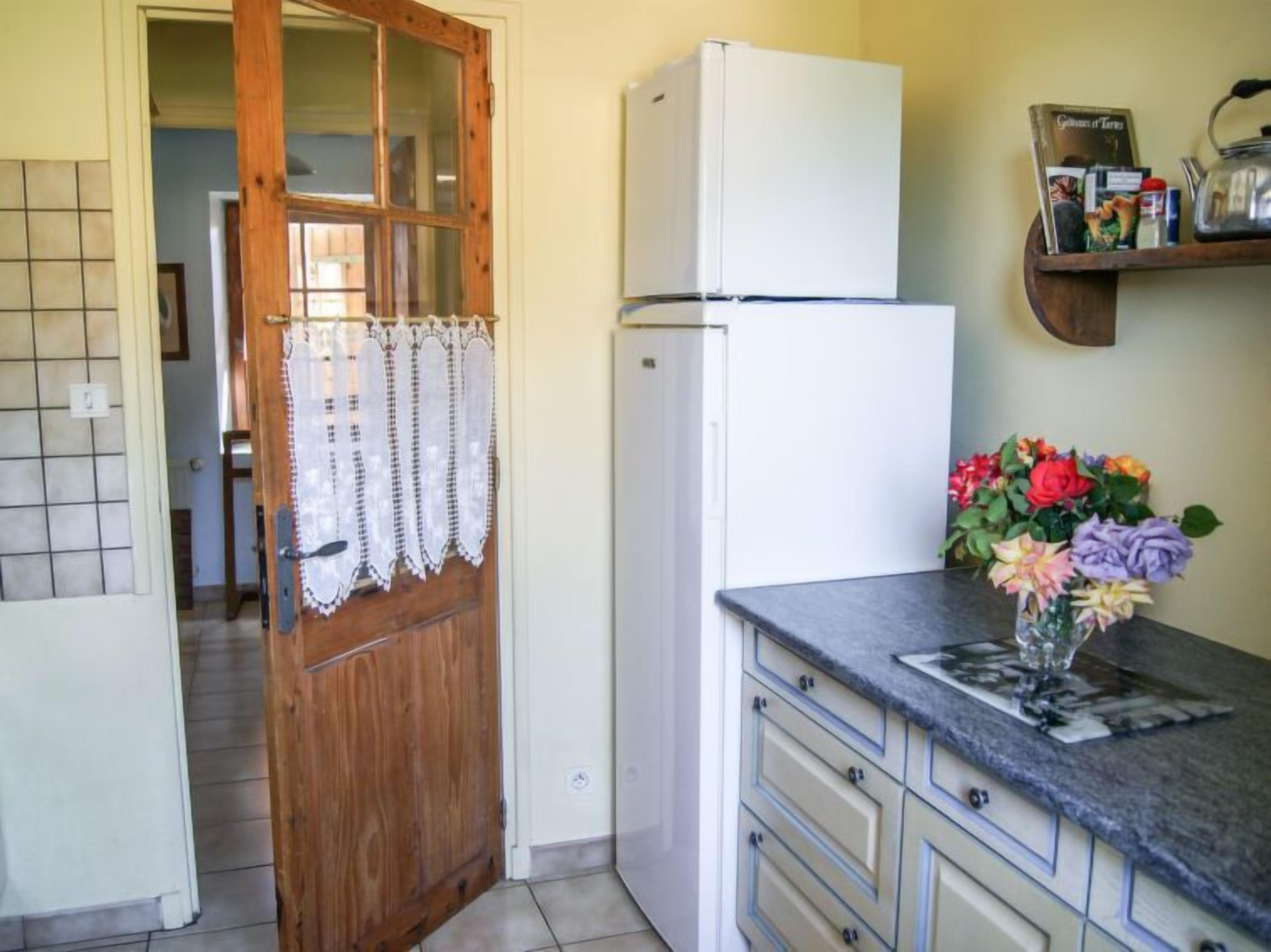 A kitchen with a wooden door, a white refrigerator, and a countertop with a vase of flowers.