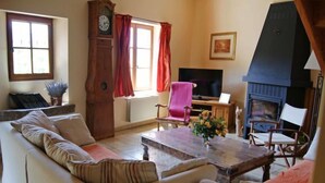 Un salon chaleureux avec un canapé, une table basse en bois, une cheminée, un téléviseur et une horloge.