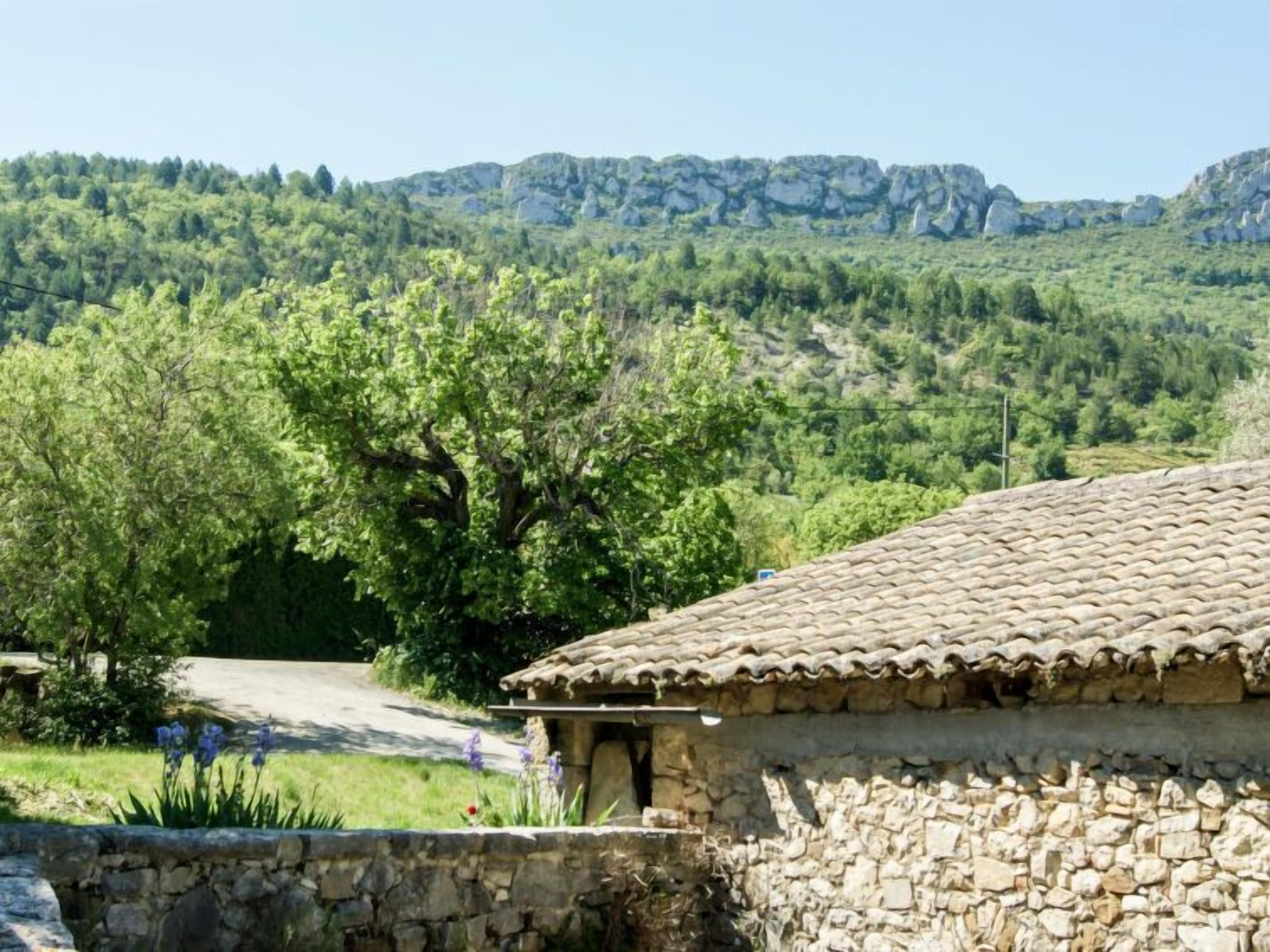 A stone building with a tiled roof, surrounded by greenery and a mountainous backdrop.