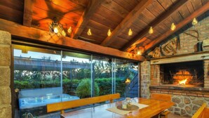 An outdoor dining area with a wooden table and benches, a stone fireplace, and a glass enclosure with a view of greenery. - Rukavina by Interhome (Senj)