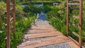 A wooden pathway leading through a garden with various plants and flowers. - Rukavina by Interhome (Senj)