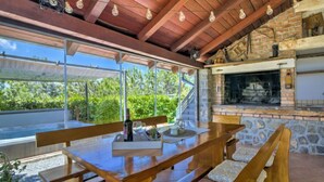 An outdoor dining area with a stone fireplace and a view of greenery. - Rukavina by Interhome (Senj)