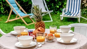 Ulkona katettu aamiaispöytä, jonka päällä on ananas, croissant-leivoksia ja appelsiinimehua.