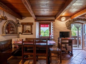 A rustic interior with a wooden dining table, benches, a TV, and a stone wall.