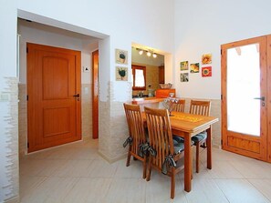 A dining area with a wooden table and chairs, a kitchen in the background, and a large mirror above the table.
