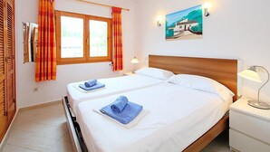 Een tweepersoonsbed met witte lakens, twee nachtkastjes met lampen, een schilderij aan de muur en een raam met gordijnen.