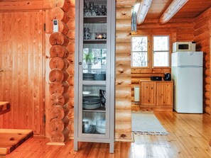 A wooden cabin interior with a central glass-fronted cabinet, wooden walls, a refrigerator, and a window with a view.