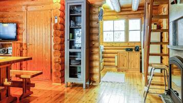 A log cabin interior with a wooden dining table, a built-in bookshelf, a fireplace, and a window with a view.