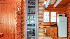 A log cabin interior with a wooden wall, a glass-fronted cabinet with dishes, a microwave, and a refrigerator.