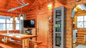A log cabin interior with a wooden dining table, benches, a television, and a cabinet with glass doors.