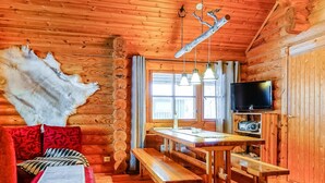 A log cabin interior with a wooden dining table, benches, a red sofa, a television, and a large fur rug.