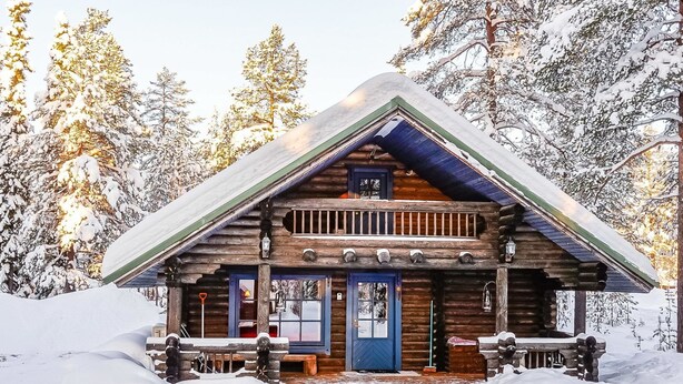 A log cabin with a front porch, surrounded by snow-covered trees.