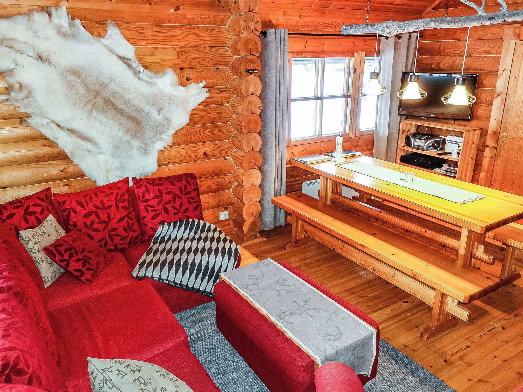 A log cabin interior with a sofa, pillows, a dining table, and a television.