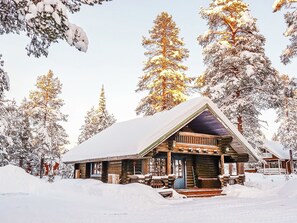 A log cabin with a snow-covered roof, surrounded by snow-laden trees. - Tikkatupa by Interhome (Kittilä)