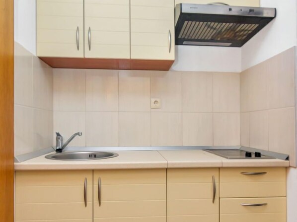 Una cocina con armarios color beige, un lavamanos de acero inoxidable y una campana extractora negra.