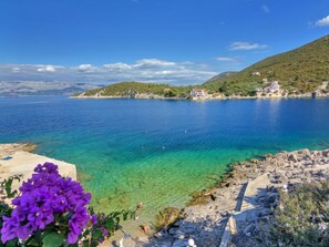 Un paisaje costero con aguas azules cristalinas, una costa rocosa y una colina distante con edificios.