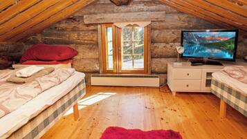 Un dormitorio acogedor en el ático con techo inclinado de madera, un ventanal grande, un televisor y dos camas con ropa de cama a cuadros.