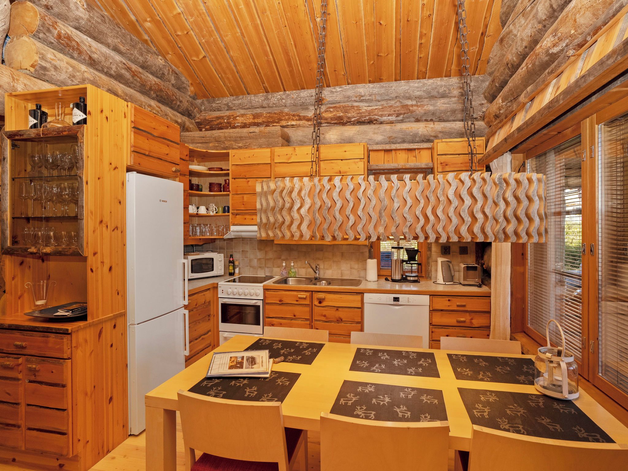 Cocina rústica de cabaña con armarios de madera, un refrigerador Bosch, un microondas, un lavamanos y un comedor con mesa y sillas.