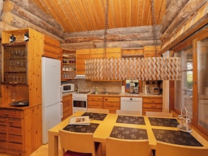 Cocina rústica de cabaña con armarios de madera, un refrigerador Bosch, un microondas, un lavamanos y un comedor con mesa y sillas.