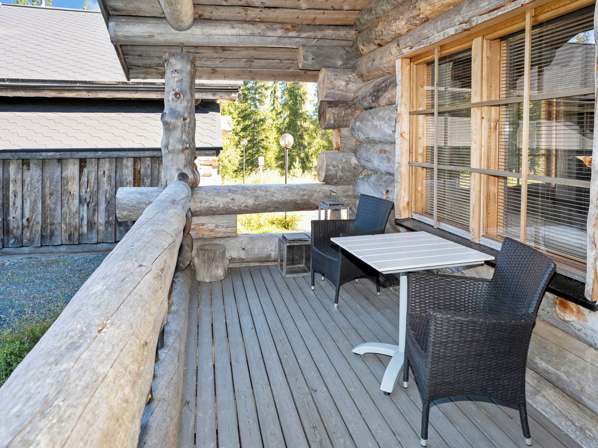 Une terrasse extérieure en bois, avec une table et des chaises, une clôture en bois et une fenêtre avec des stores.