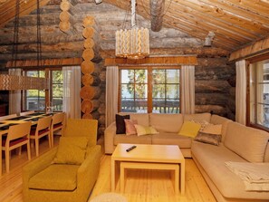 Interior de una cabaña de troncos con una mesa de comedor de madera, sillones amarillos, un sofá y una lámpara colgante.