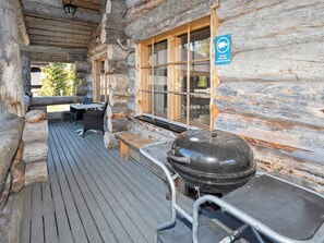 Une cabane en rondins avec une terrasse en bois, un barbecue et une table avec des chaises.