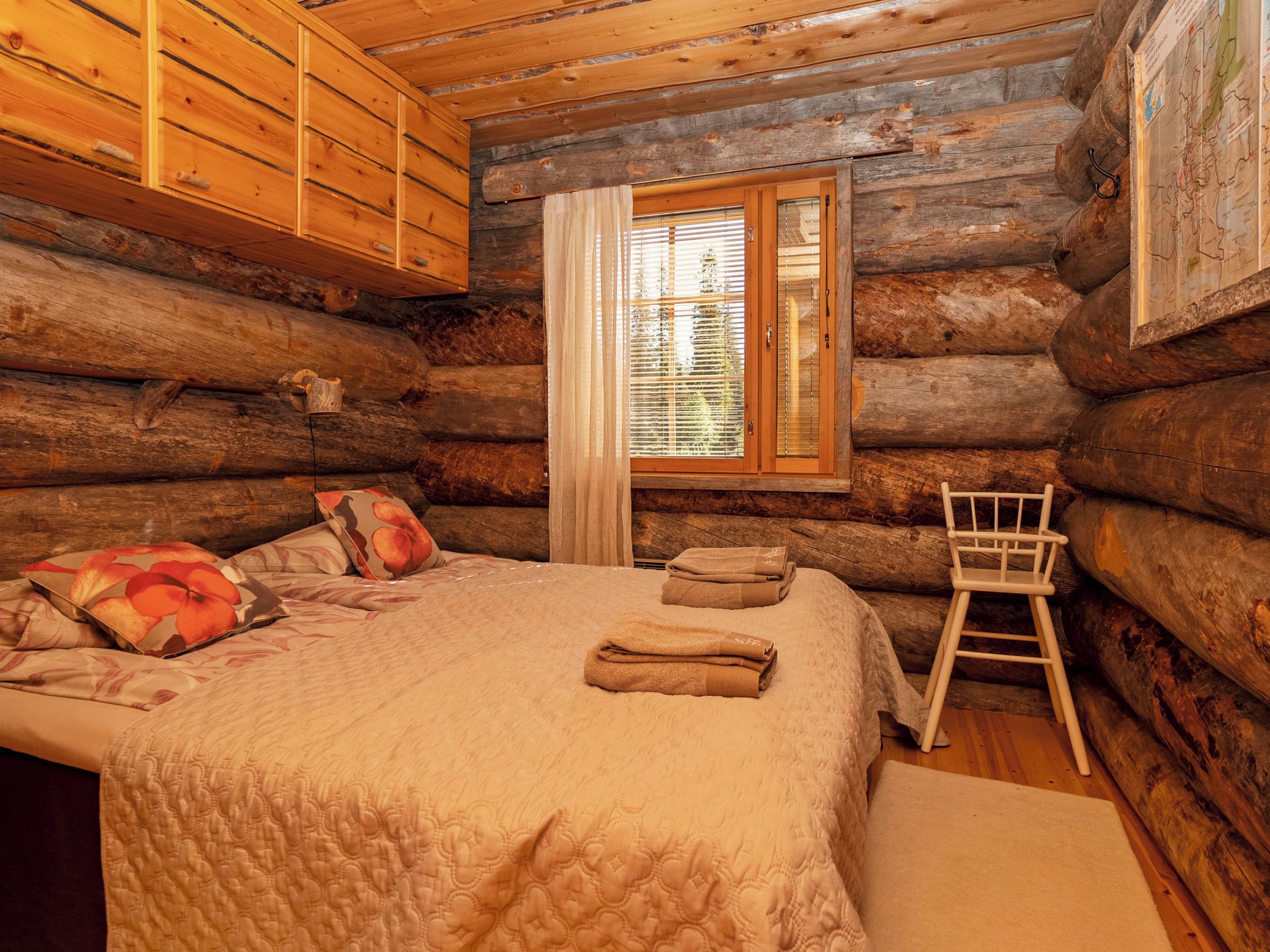 A log cabin room with a bed, a chair, and a window with blinds.