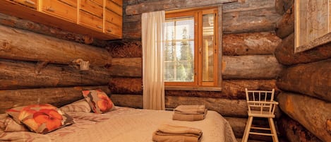 A log cabin room with a bed, a chair, and a window with blinds.