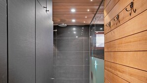 Un baño moderno con cabina de ducha de vidrio, paredes de azulejos oscuros y paneles de madera en una pared.