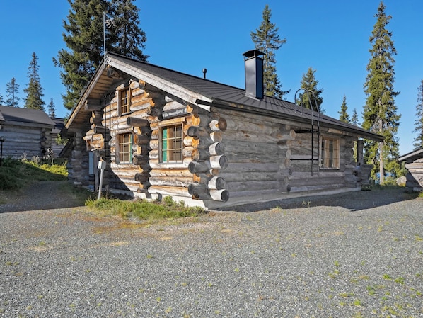 A log cabin with a steeply pitched roof, a chimney, and a gravel driveway.