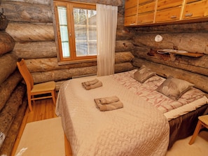 Un dormitorio de cabaña de troncos con una cama, una silla y una ventana con persianas.