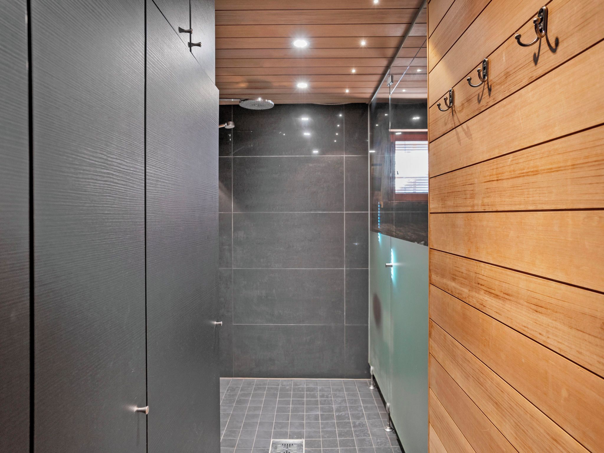 Ein modernes Badezimmer mit Dusche, gefliestem Boden und Holzvertäfelung an einer Wand.