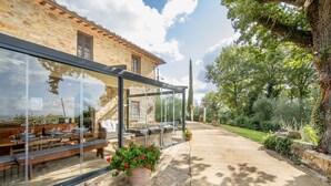 Un edificio de piedra con un patio cubierto de vidrio, mobiliario exterior y un sendero de jardín.