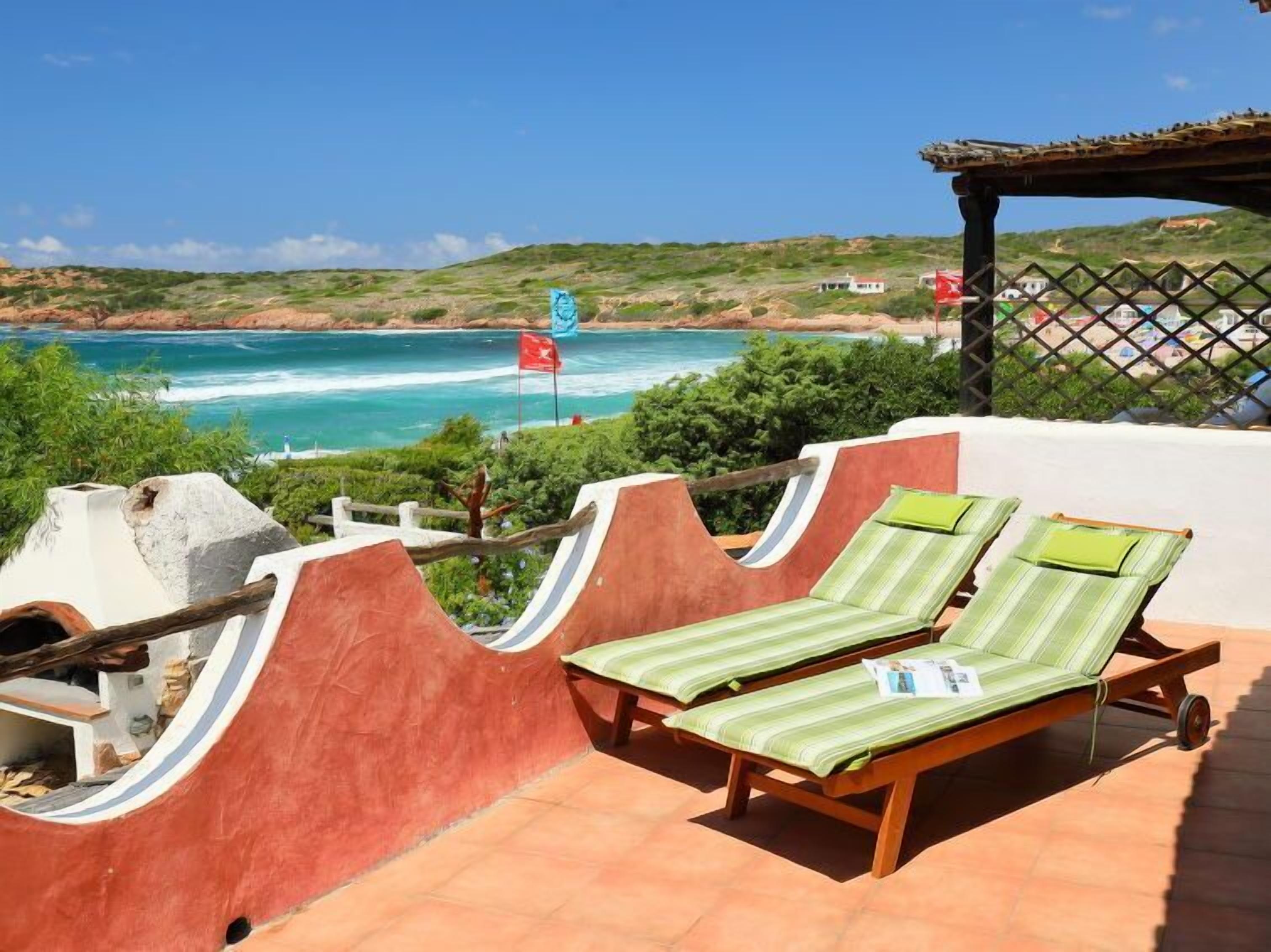 A terrace with two sun loungers, a view of the sea, and a flag.