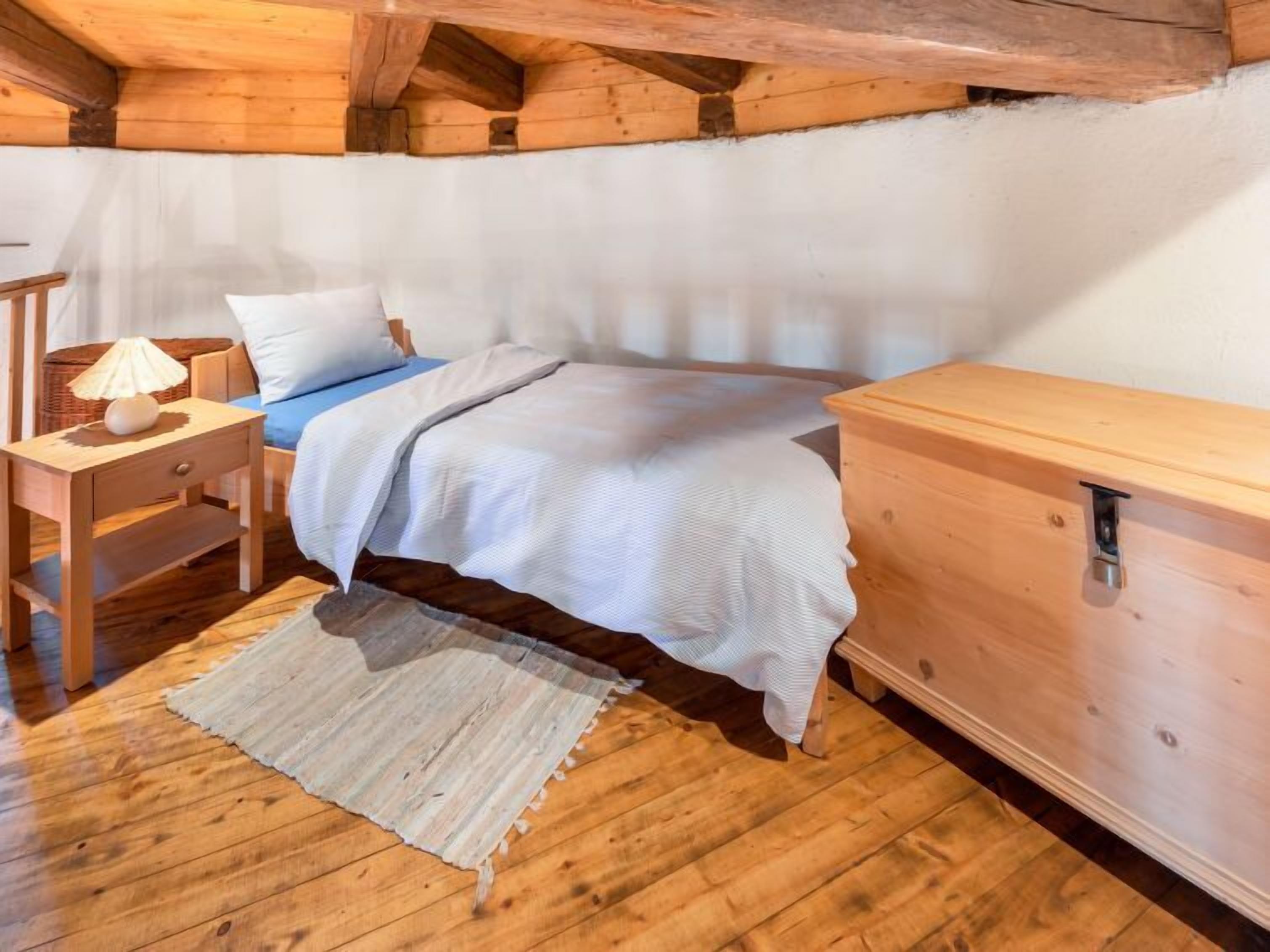 Ein gemütliches Schlafzimmer mit einem hölzernen Bett, einem Nachttisch, einer Lampe und einer Holzkommode.