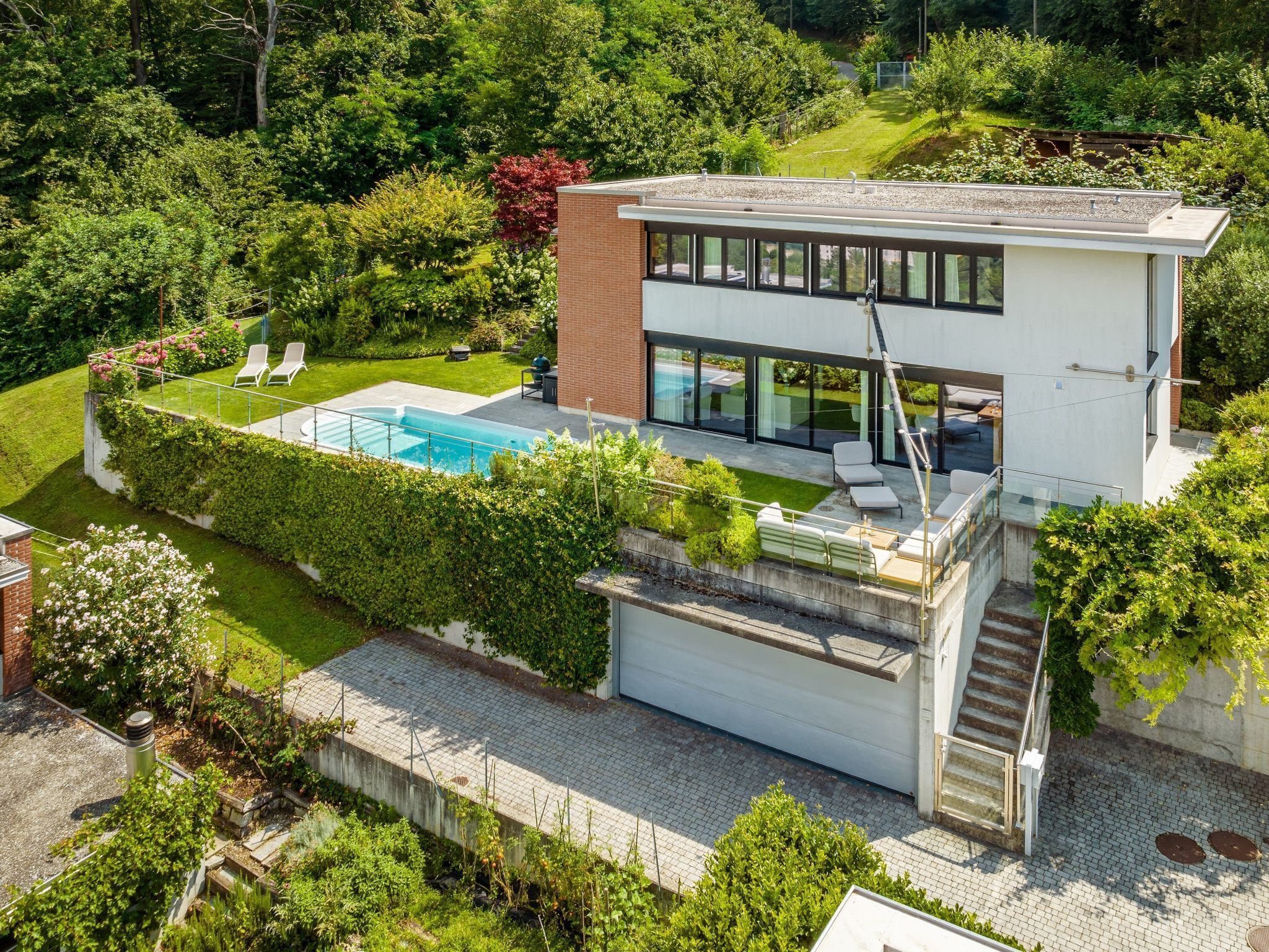 Ein modernes Haus mit Schwimmbad, überdachter Terrasse und einer Treppe, die zur Garage führt.